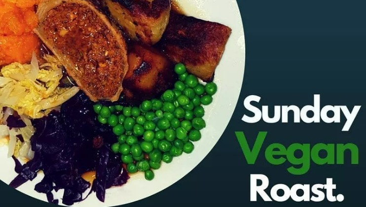 A plate with a Sunday vegan roast, featuring roasted vegetables, peas, red cabbage, mashed sweet potato, and a vegan roast centerpiece. Text on the image reads Sunday Vegan Roast. in white and green font against a dark background.