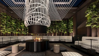 Modern outdoor lounge area with a central circular fire pit, surrounded by cushioned benches in a checkered pattern. Above the fire pit is an intricate, artistic light fixture. The space features vertical greenery along the walls, creating a cozy ambiance.