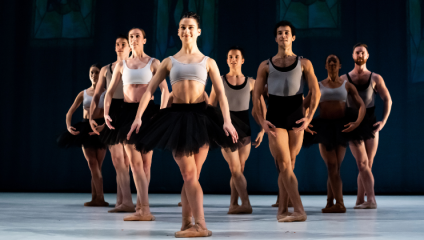 A troupe of dancers from Ballet Cymru pose cross-legged, arranged in a V formation