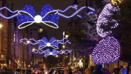 Blue and white Christmas lights, taking the shape of bows, light up the night sky above a busy shopping street in Belgravia.