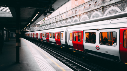 A Circle Line Underground train whizzes down the line one track over from the station platform; while the train is illuminated by the daylight, the platform is shrouded in darkness.