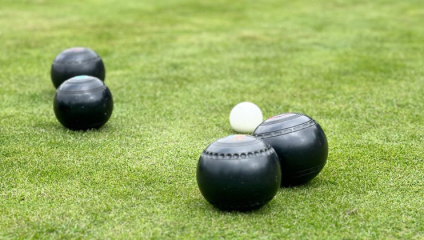 On a crisp green lawn, four large black bowls balls surround one small white ball