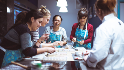 A group of women lean over a metal table making chocolates in a workshop at Cocoa Crystal in Brighton