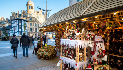 The view from inside a row of Christmas market stalls, looking out at Manchester city during the daytime