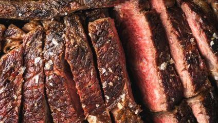 Close-up of a sliced, juicy, medium-rare steak with a crisp, seared crust. The meat is garnished with coarse sea salt, showcasing varying shades of brown on the outside and pink to red on the inside. The texture appears tender and flavorful.