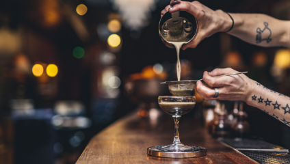 A close-up shot, from the side, of tattooed forearms mixing a cocktail at London's Little Bat Bar in Islington