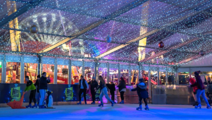 The indoor ice rink at Trafford Centre in Manchester. Beyond the rink, we can see a winter wonderland, with ferris wheel, in the background.