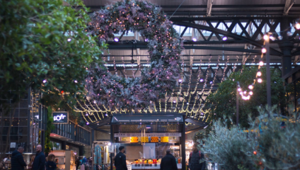 A huge Christmas wreath and other greenery are suspended from the ceiling of Old Spitalfields Market, surrounded by hundreds of Christmas lights.