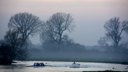 On a wintery day, team of rowers row through the river in Port Meadow, Oxford