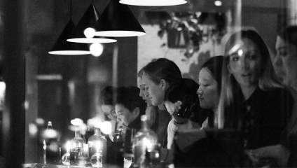 A black-and-white shot through the window of Soho's Paradise: After Dark bar; people are smiling and socialising over drinks