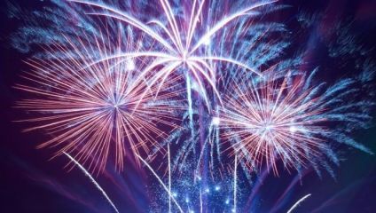 A vibrant display of fireworks lights up the night sky with bursts of blue, purple, and pink hues. The intricate patterns of light create an enchanting and celebratory atmosphere.