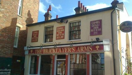 The front facade of The Bricklayer's Arms pub in London. The cream-colored building features red signage indicating awards from CAMRA for best London Pub of the Year in 2006-2009 and Southeast London Pub of the Year in 2010. A Guinness sign hangs nearby.