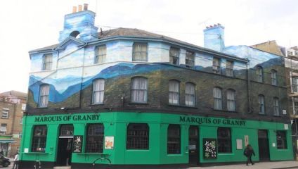A corner pub named Marquis of Granby with a bright green lower facade and mural depicting a mountainous landscape on the upper portion of the building. The pub has multiple chimneys and windows, with surrounding urban buildings visible in the background.
