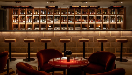 The sleek bar at London's Seed Library bar, behind a group of deep red suade chairs centered around a red table