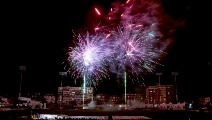 Two green laser beams shoot skyward from Sussex Cricket Ground, each ballooning into a giant fireworks explosion of purple and red jets of light