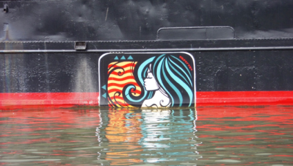 A colorful mural partially submerged in water on the side of a dark-colored boat. The mural features a stylized profile of a woman with flowing blue and green hair against a red, orange, and yellow wavy background.