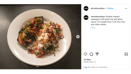 A plate of food featuring stuffed roasted aubergine with lentil rice and tahini sauce, garnished with chopped vegetables and herbs. The dish is on a round white plate, presented on a dark surface. The image is from an Instagram post by almeidacafebar.