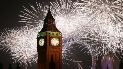 Big Ben illuminated at night with vibrant fireworks lighting up the sky behind it, creating a spectacular display. The London Eye can be seen in the background amidst the fireworks, adding to the festive atmosphere in London.