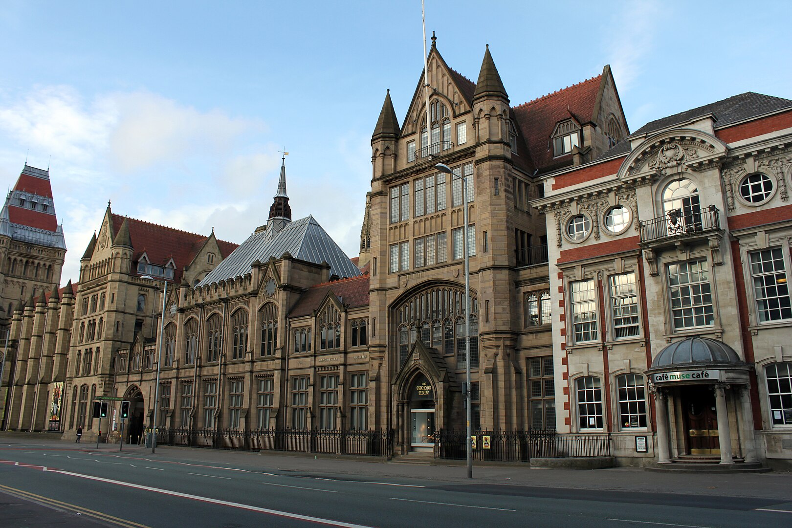 The exterior facade of Manchester museum. The entrance to the museum cafe is shown and the sky is blue with a few white clouds