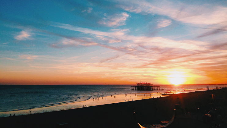 A spectacular sunset over the ruined West Pier on Brighton beach with the clouds a vibrant mix of oranges and red contrasting against the azure sky with the sand and promenade in shade in the foreground