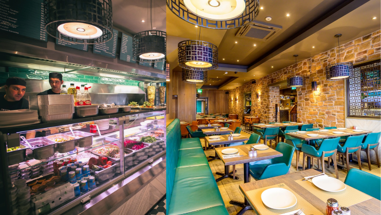 A vibrant Mediterranean restaurant with a display of fresh salads and dishes on the left and a seating area with turquoise chairs and wooden tables on the right. The walls are adorned with stone tiles, and the ceiling has modern, decorative light fixtures.