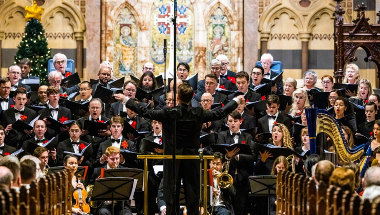 A professional choir of carol singers is led by the conductor in a grand and beautiful church