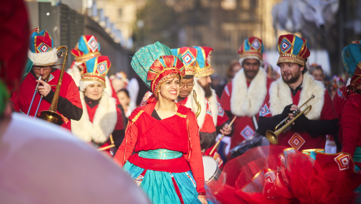 Performers in bright and colourful red and green Christmas costumes, some with trumpets, walk the streets of Manchester as part of the Manchester Christmas Parade