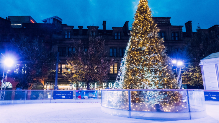 An outdoor ice rink, at night, with a huge Christmas tree in the middle