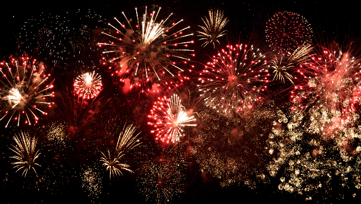 A vibrant display of fireworks illuminates the night sky. Various bursts of red and gold fireworks explode in an array of shapes and sizes, creating a stunning spectacle of color and light. The dark background enhances the vividness of the fireworks.