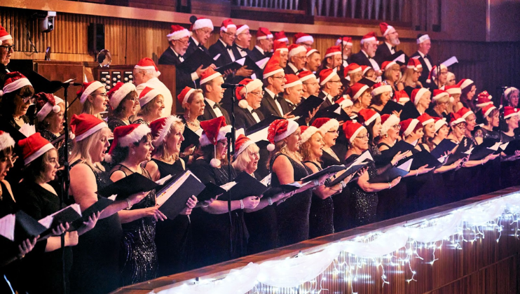 A choir, all wearing Santa hats, sing carols from the gallery in Manchester’s international concert venue The Bridgewater Hall