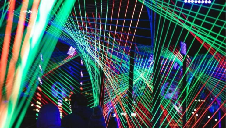 A man walks through the Christmas Trail at Wilderspool Woods in The Trafford Centre; differently-coloured lines of light twist around the path above him