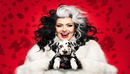 A person with dramatic black and white hair, a white fur coat, and bright red lipstick smiles while holding a Dalmatian puppy. The background is red with black spots, echoing the Dalmatian's pattern.