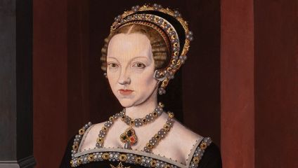 A historical portrait of a woman with pale skin and blonde hair, styled in an intricate updo adorned with pearls and gold. She wears a black dress with detailed embroidered patterns and jeweled accessories, including a necklace with a prominent red gemstone.