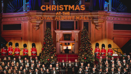 Looking down at the Royal Choral Society performing at The Royal Albert Hall. A sign made up of Christmas lights behind them reads: Christmas at the Royal Albert Hall