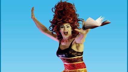 A person with dramatic makeup, wearing a flamboyant red and black sequined outfit, is posing energetically against a blue background. They have large, curly, voluminous hair and are holding an open book that appears to be floating.