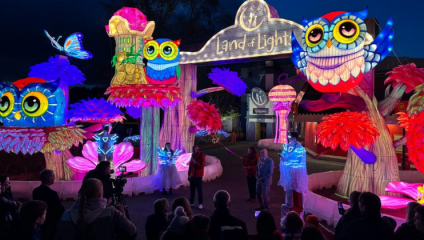 Families stand outside the entrance to the Land of Lights Festival at Gullivers World theme park in Warrington - several giant colourful light installations stand at different heights around them