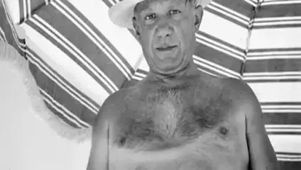 A shirtless man wearing a straw hat stands in front of a striped fabric background, possibly an umbrella or tent. The image is black and white.