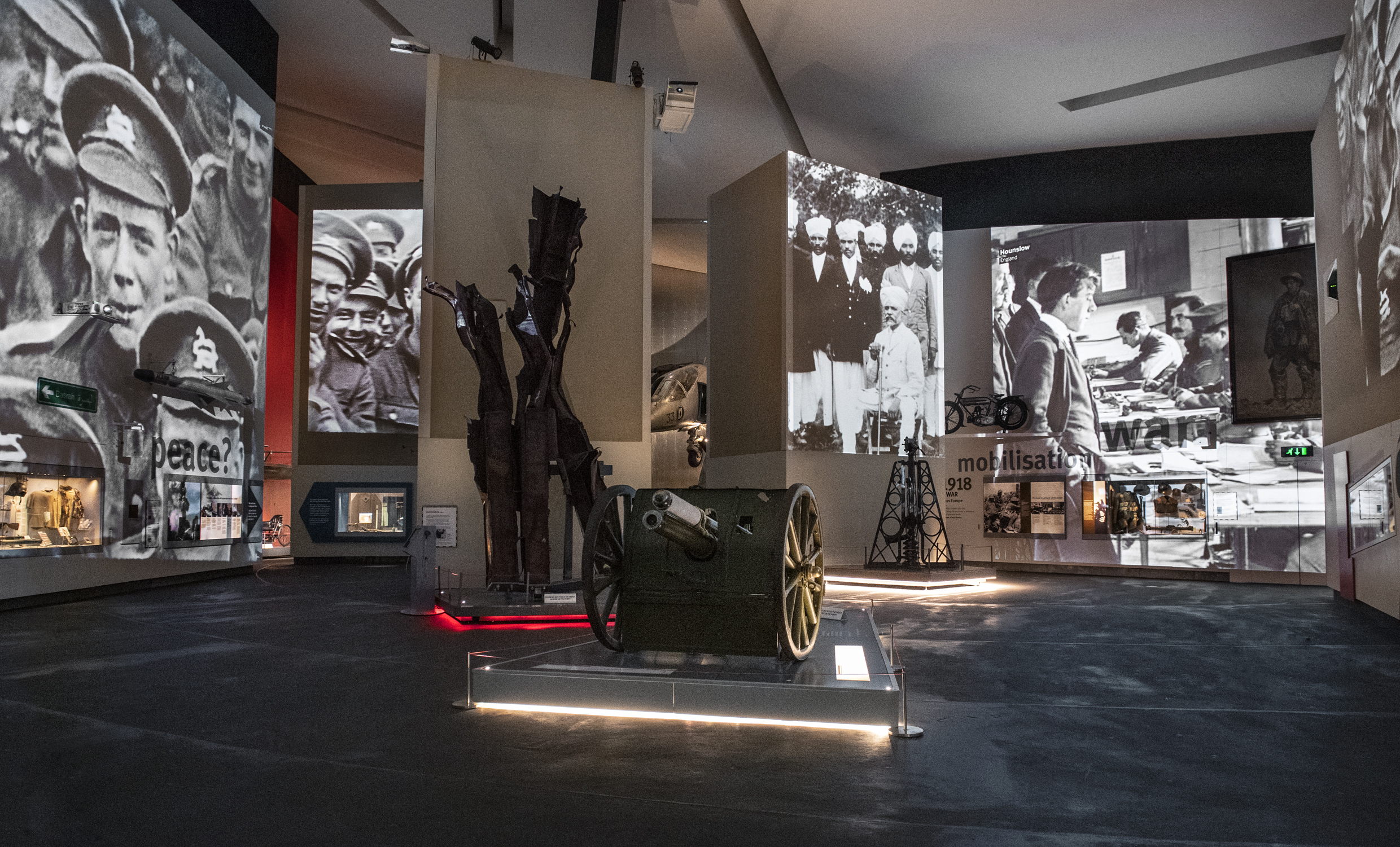 A museum exhibit showcasing artifacts and large historical photographs. Prominently displayed are a military uniform, old artillery, and vintage equipment. The walls feature enlarged black and white photos of military personnel and significant historical moments.