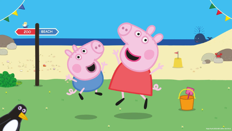 Two animated pigs, one smaller in blue and one larger in red, joyfully jump on a grassy area near a beach. A signpost points toward the zoo and beach. A penguin and a bucket with a shovel are nearby. In the background, water, sand, and rocks are visible under a clear blue sky.